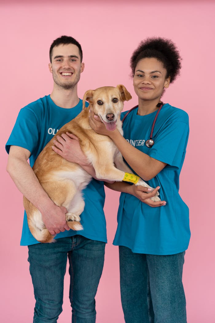 Two smiling volunteers holding a friendly dog, showcasing adoption spirit.